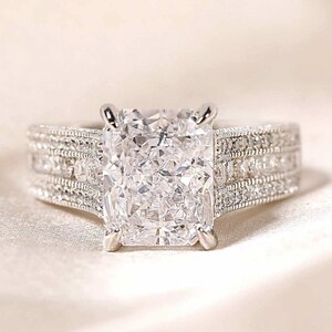 May include: A silver engagement ring with a large, square-shaped diamond center stone and smaller diamonds set in the band.