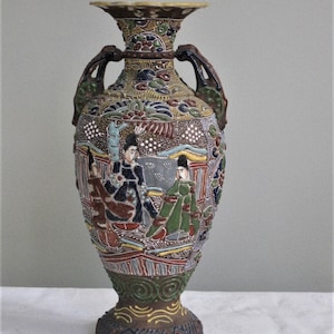 May include: A brown and white ceramic vase with a floral design and two handles. The vase is decorated with a scene of people in traditional Japanese clothing.