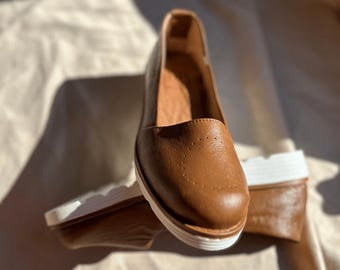 May include: A pair of brown leather shoes with white soles. The shoes have a pointed toe and a low heel.