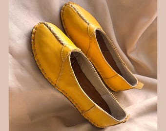 May include: A pair of yellow leather flats with a stitched edge. The shoes have a pointed toe and a flat sole.
