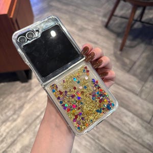 May include: A clear phone case with a glittery, liquid-filled back. The glitter is gold, red, blue, green, and purple. The case is open to reveal a black screen.