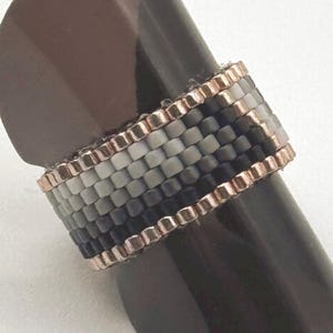 May include: A beaded ring with a gradient of gray and black beads, accented with a rose gold wire wrap.