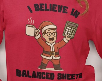 May include: Red long-sleeve shirt with the text "I Believe in Balanced Sheets." The shirt features a cartoon Santa Claus holding a coffee mug and a calculator. The Santa Claus is wearing glasses and a Santa hat.
