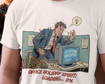 May include: White t-shirt featuring a comic illustration of a stressed office worker at Christmas. The graphic shows a computer screen with "SYSTEM UPDATE" and the text "OFFICE HOLIDAY SPIRIT: LOADING... 2%."