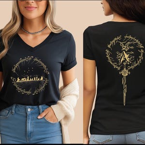May include: A black V-neck t-shirt featuring a gold graphic on the front showing a silhouette of a group of figures walking within a circular Elvish script border. The back of the shirt displays a gold graphic of a sword and a mountain scene.
