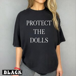 a woman wearing a black t - shirt that says protect the dolls