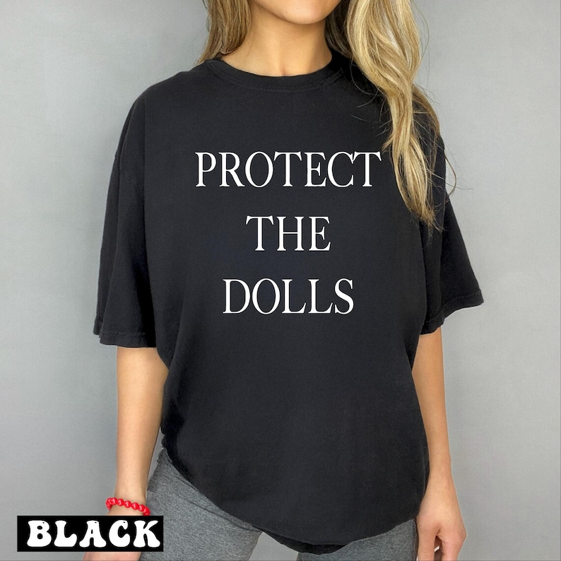 a woman wearing a black t - shirt that says protect the dolls