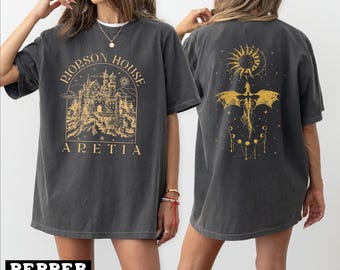 May include: Dark gray t-shirt with a gold graphic on the front and back. The front features text and a castle illustration. The back has a sun, moon, and dragon design. The shirt is a casual, oversized fit.