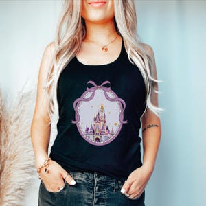 A woman with long blonde hair wearing a black tank top with a castle graphic on it.