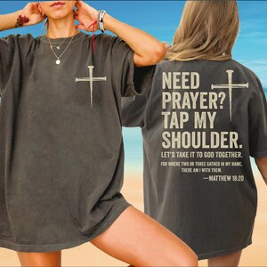 a person wearing a gray t-shirt with a Bible verse printed on the back.