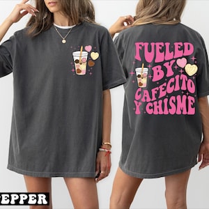 May include: A dark gray oversized t-shirt with a pink graphic on the front of a coffee cup with hearts and a pink graphic on the back that says "Fueled by Cafecito y Chisme".