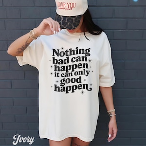 May include: Ivory-colored oversized t-shirt with the text "Nothing bad can happen it can only good happen" in black. The shirt is paired with a white baseball cap with the text "I LOVE YOU" in red. The cap has a leopard print brim.