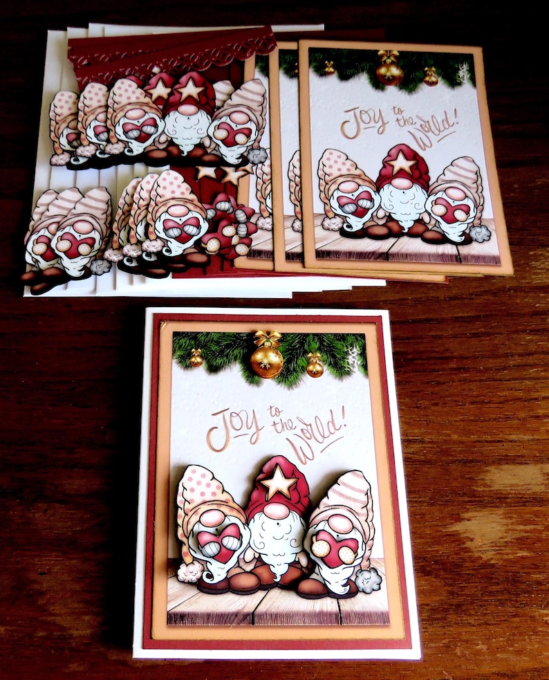 May include: Christmas-themed greeting cards featuring gnome illustrations. The cards have a white background with the phrase "Joy to the World!" and are decorated with festive elements like ornaments and greenery. The gnomes wear red and beige hats.