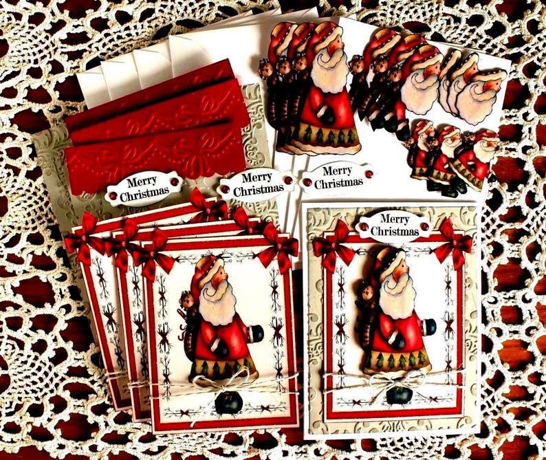 Op de afbeelding: Een set handgemaakte kerstkaarten met een centrale illustratie van de Kerstman in een rode jas, versierd met rode strikken, touw en een Merry Christmas-label, inclusief bijpassende witte enveloppen en rood reli&euml;f karton.