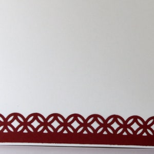 May include: A white card with a decorative, burgundy-colored border. The border features a repeating pattern of interlocking circles. The card is blank, offering space for a personalized message or design.