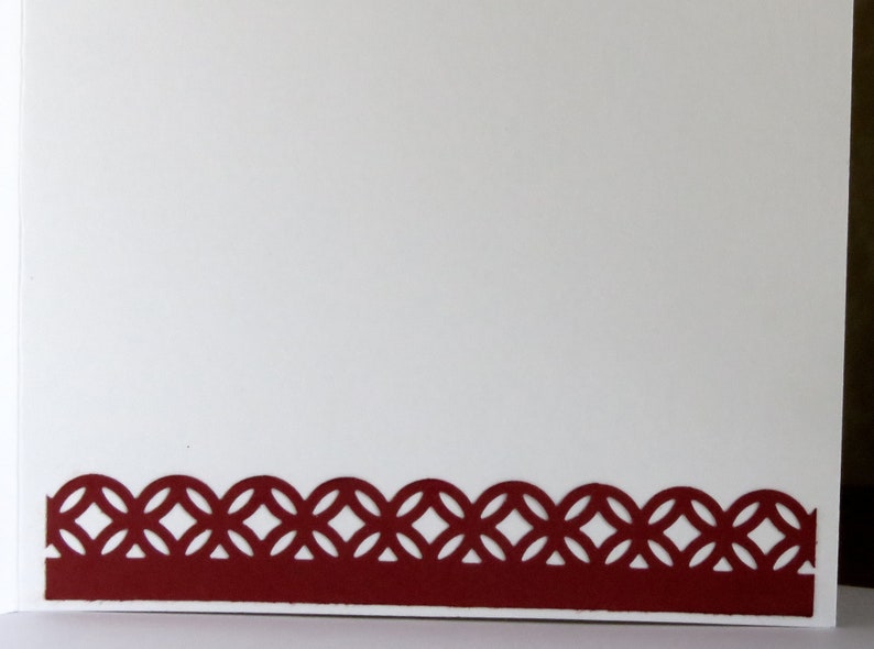 May include: A white card with a decorative, burgundy-colored border. The border features a repeating pattern of interlocking circles. The card is blank, offering space for a personalized message or design.