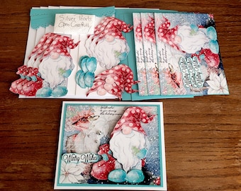 May include: A set of five greeting cards featuring a winter gnome design. The cards are decorated with snowflakes, poinsettias, and the text "Winter Wishes". The cards are packaged with a blue and white patterned envelope and a tag that reads "Silver Pearls Open Carefully".