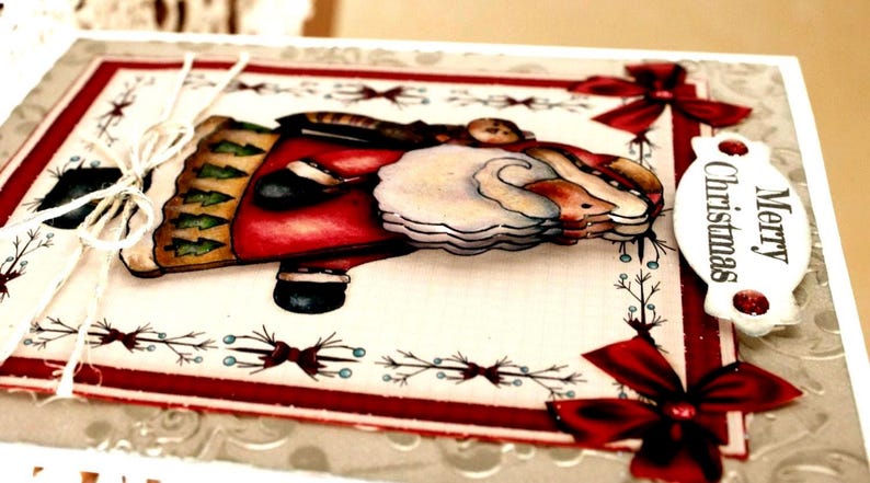 Op de afbeelding: Een handgemaakte wenskaart met een gelaagde, driedimensionale illustratie van de Kerstman in een rode jas met een witte baard. De kaart heeft een cr&egrave;mekleurige achtergrond, rode randen, decoratieve rode strikken en een label met Merry Christmas.