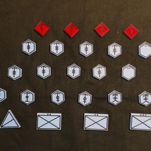 Könnte beinhalten: Ein Satz weißer und roter Spielsteine mit verschiedenen Symbolen. Die Steine sind in einem Gittermuster auf einem braunen Stoffhintergrund angeordnet.