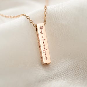 May include: Rose gold bar pendant necklace with the inscription "Sleep in heavenly peace" and the name "Dawn" and the date "December 15th, 2023" engraved on the bar. The pendant hangs from a delicate chain.