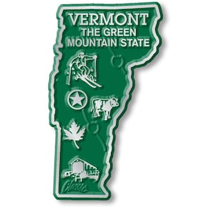 May include: A green and white magnet shaped like the state of Vermont. The text "VERMONT THE GREEN MOUNTAIN STATE" is displayed. Illustrations include a skier, star, cow, maple leaf, and barn. The magnet is approximately 10 cm tall.