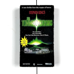 May include: A VHS tape for Stephen King's "The Tommyknockers" miniseries. The cover features a dark background with green and white text, a glowing green light, and a rural town scene. The text includes "You Can't Run. You Can't Hide. You Can Only Become... One Of Them."