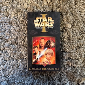 May include: A VHS tape of "Star Wars: Episode I - The Phantom Menace." The black tape case features the movie title in gold and a collage of characters. The bottom of the case reads "Digitally Mastered for Superior Sound and Picture Quality."