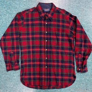 Może przedstawiać: Koszula flanelowa w kratę czerwoną, zieloną i niebieską z kołnierzykiem zapinanym na guziki i długimi rękawami.