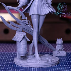 May include: A gray 3D-printed figurine of a character with a pleated skirt, holding a large weapon. The figurine includes a lantern, a small animal figure, and the text "Lullaby's 3D Print". The base is round and detailed.