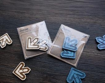 May include: Two packages of arrow magnets, one with blue arrows and one with brown arrows. The packages are on a dark wood surface. The packages have the words "Arrow Magnets" printed on them.