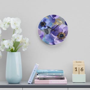 May include: A round wall clock with a floral design featuring purple and blue watercolor flowers on a gray background. The clock hands are black.