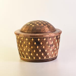 May include: A handcrafted wooden box with a domed lid. The box is made of dark brown wood with inlaid diamond-shaped accents in a lighter wood. The lid and body feature a repeating geometric pattern. The box is a decorative storage container.