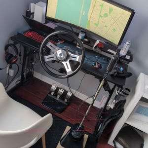 Peut inclure: Un volant de course noir avec un centre argenté et un revêtement en cuir noir pour le volant. Le volant est monté sur un support noir avec un levier de vitesses noir et vert. Le volant est connecté à un moniteur d'ordinateur affichant une carte. La configuration est sur un bureau noir avec un clavier noir et une souris noire.