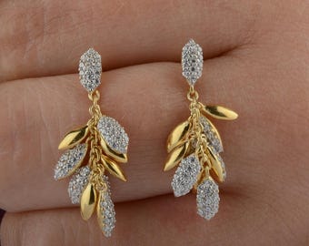 May include: A pair of drop earrings featuring a cluster of gold-toned metal leaves and pavé-set crystal leaves. The design includes alternating smooth gold-colored metal segments and textured, sparkling crystal-encrusted segments hanging from a post.