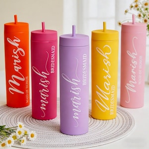 Könnte beinhalten: Fünf bunte Becher mit Strohhalmen. Die Becher sind in den Farben Orange, Pink, Lila, Gelb und Pink gehalten. Jeder Becher trägt den Namen "Marish" in weißer Schrift. Einige Becher tragen die Aufschrift "Brautjungfer".
