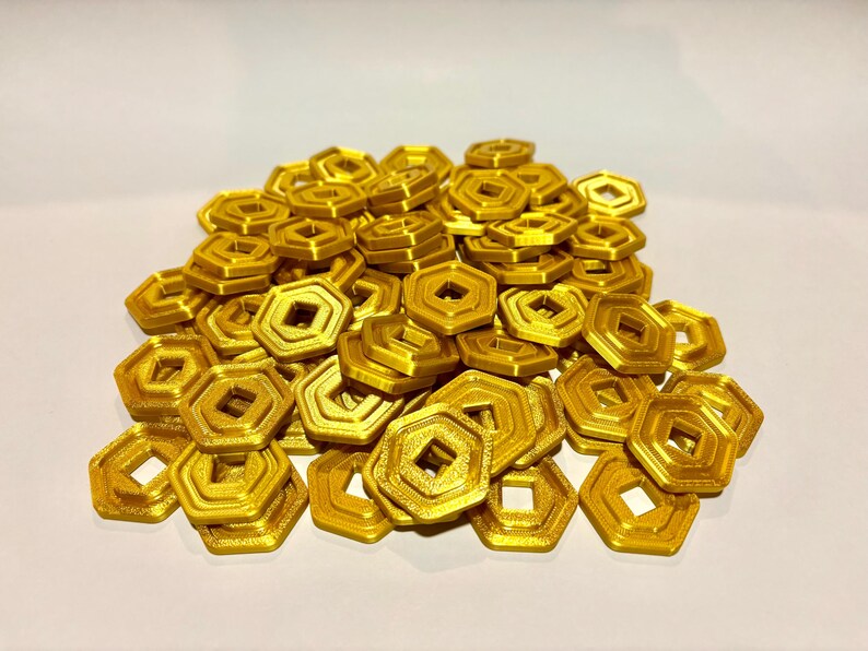 May include: A pile of gold-colored, hexagonal, plastic tokens with a square hole in the center.
