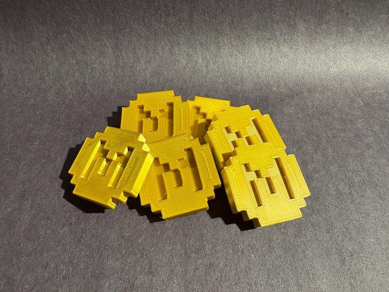 May include: A group of six gold-colored plastic coins with a pixelated design. Each coin has a raised design of three horizontal lines.