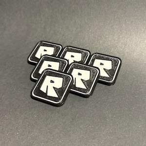 May include: Six black square-shaped patches with a white letter "R" in the center. The patches are stacked on top of each other.