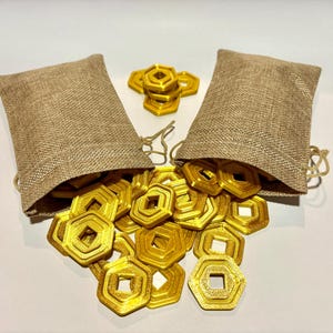 May include: Two burlap bags filled with gold-colored metal coins. The coins are shaped like octagons with a square hole in the center. The coins are spilling out of the bags onto a white surface.