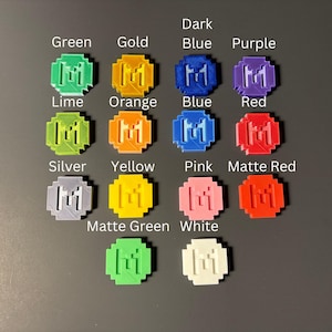May include: A set of 14 round, plastic, 3D printed tokens in various colors, including green, gold, dark blue, purple, lime, orange, blue, red, silver, yellow, pink, matte red, matte green, and white. Each token features a stylized letter "M" in the center.