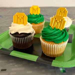 May include: Four cupcakes decorated with green frosting and gold Minecraft-themed toppers on a green and black Minecraft-themed paper plate.
