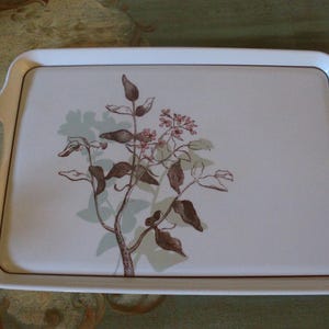 May include: Rectangular white serving tray with integrated handles. The tray features a floral design with brown leaves and pink flowers on a light beige background. The tray has a thin brown border.