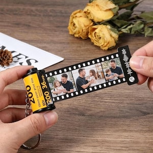 May include: A personalized keychain featuring a film roll design. The yellow film canister has "200" and "36 exp." printed on it. A strip of film displays three family photos. The keychain is held by a person's hand.