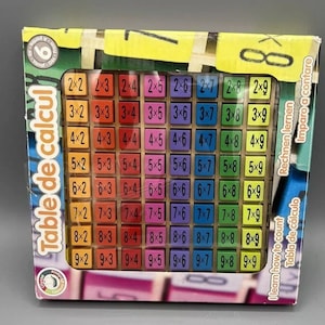 Peut inclure: Jeu de table de multiplication coloré dans une boîte. Le jeu présente une grille de problèmes de multiplication, avec les réponses affichées sur des tuiles individuelles. La boîte contient du texte en plusieurs langues, dont « Table de calcul ».