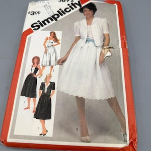 Puede incluir: Un patrón de costura Simplicity vintage que muestra a una mujer con un vestido blanco y una chaqueta a juego, y un conjunto de falda y chaqueta negros. La portada del patrón es roja y blanca.