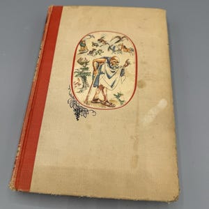 May include: A hardcover book with a beige fabric cover and a red spine. The front cover features a central oval illustration of a bearded figure in a white robe holding a staff, surrounded by various animals, with a small black grape vine graphic.