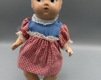 Bambola vintage anni '50 da 20 cm con occhi che guardano di lato, capelli modellati e vestito a quadretti.