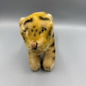 May include: A vintage plush tiger toy with a yellow and black striped pattern. The toy has a tan muzzle, small black stripes, and yellow eyes. The tiger is standing on all fours.
