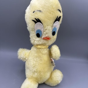 May include: A vintage Tweety Bird plush toy. The plush is yellow with black accents, large white and blue eyes, and an orange beak. It has a yellow ribbon around its neck and a tag attached to its side. The plush is in a walking pose.