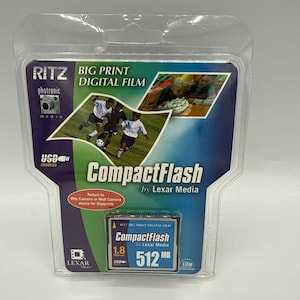 May include: A CompactFlash memory card by Lexar Media, packaged in a clear plastic case. The card has a capacity of 512 MB and features the Ritz Big Print Digital Film logo. The packaging includes images of people and the text "USB Enabled".